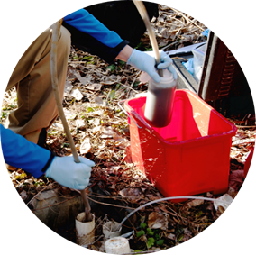 A photo of a person’s hands and a red bucket collecting a groundwater sample from a well.