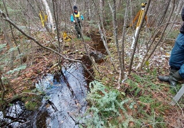 Photo of two men in the forest by stream with survey equipment.