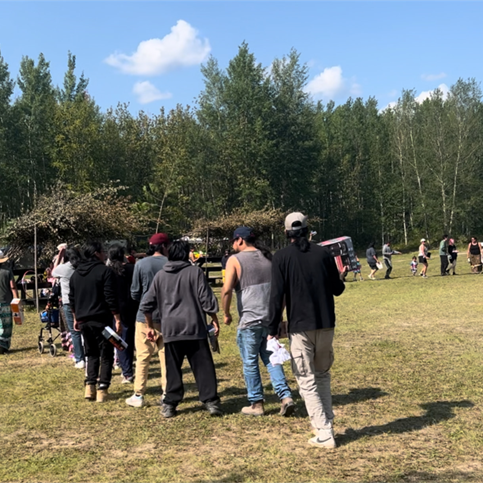 Photo of a line up of people in a grass field with trees in the background.