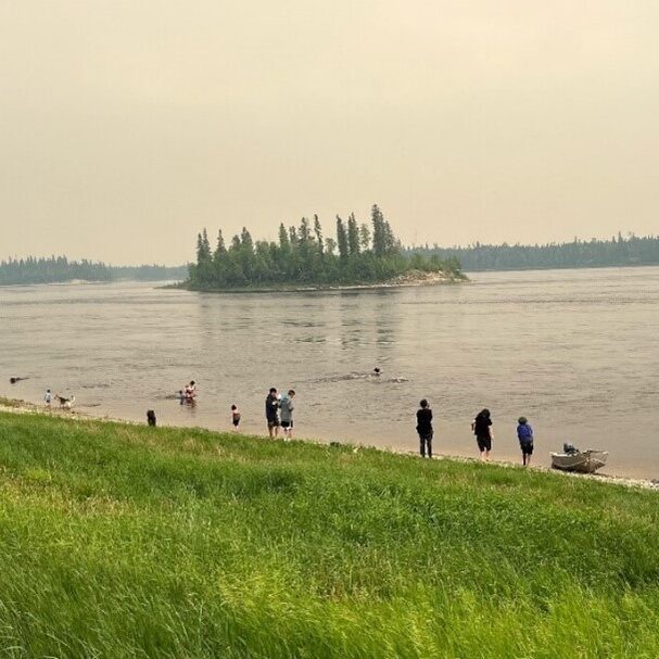 1. Photo of a group of people on a beach by a lake with an island with trees in the background.